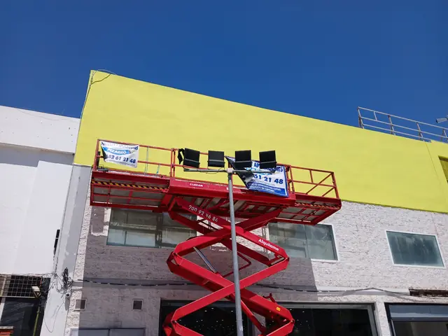 Plataforma elevadora con la lona de Pinturas y Aplicaciones Pizarro en una fachada comercial